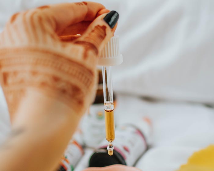 an image of a hand with a henna tattoo squeezing a tincture dropper full of CBD oil