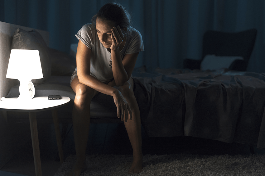 image of woman unable to sleep and up late at night stressed while sitting on her bed for the blog about What's Really in Sleep Gummies: Exploring Ingredients and Alternatives | CBD gummies for sleep | CBN for sleep