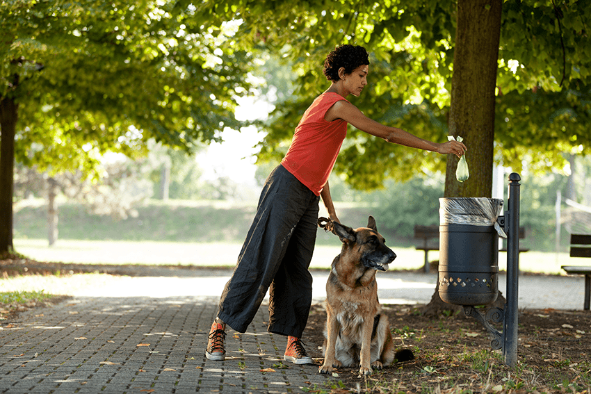 image of a woman with her dog dispensing trash at a dog park for the blog about Dog CBD for Safe and Healthy Dog Park Experiences | CBD for Dogs | Dog Parks | Pet CBD