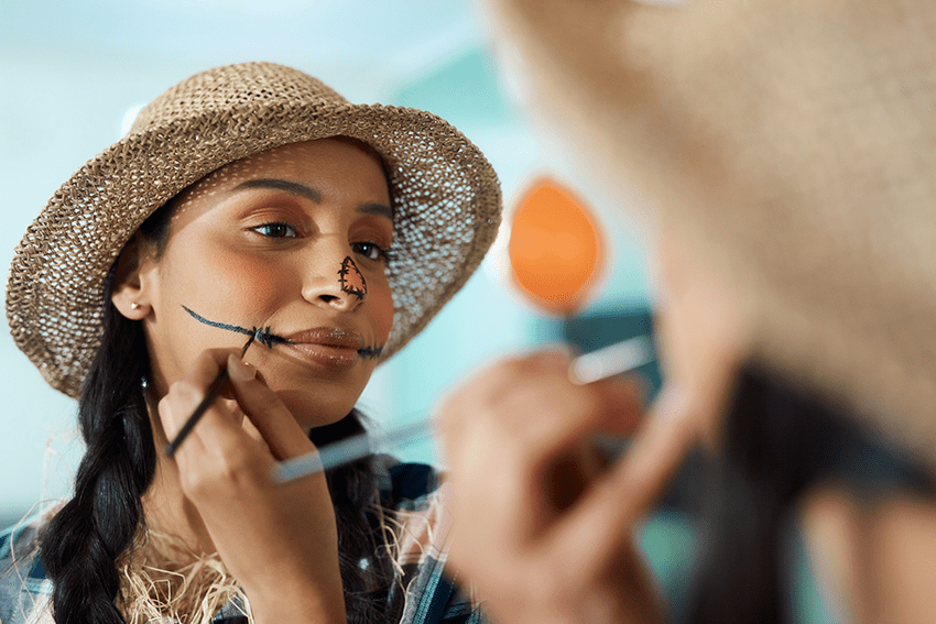 image of a woman painting a scare crow makeup look on her face for halloween for blog about CBD-Paired Halloween Costumes: Unmasking Perfect Matches