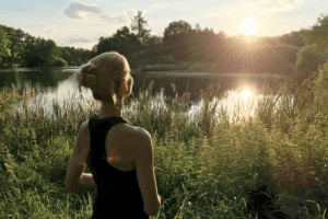 image of a woman admiring the sunset and scenery in front of a lake and trees for blog about Cultivating Growth: Enhancing Self Reflection and Confidence with CBD