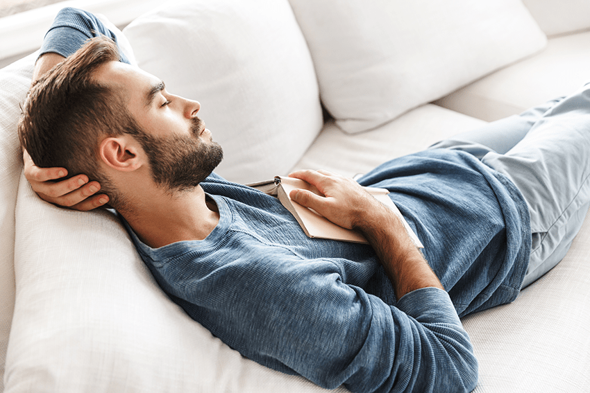 Extract Labs Holiday Gift Guide 2023 17 image of a man taking a nap on a couch with a book on his chest for blog about Extract Labs Holiday Gift Guide 2023 | CBD Gifts | Pet Gifts | Dog Gifts | Cat Gifts | Gifts for Cat lovers | Gift guide 2023