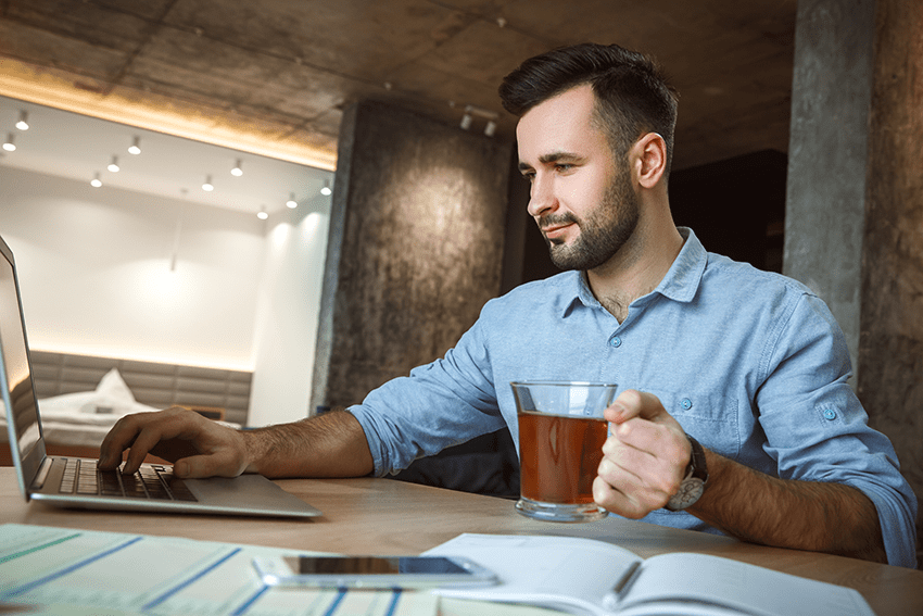 image of man working on laptop while holding a cup of tea for blog about Finding Balance Amidst Chaos: Integrating CBD into Daily Routines