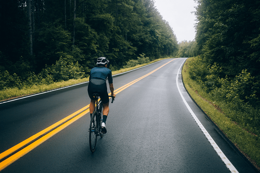 image of person biking down a road surrounded by trees for blog about Elevate Your Game: CBD Products for Athlete Performance | Best workout supplement for men | best recovery supplement | athletic performance