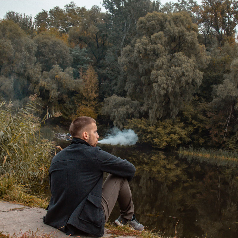 an image showing the versatility of cbd dabs, man blowing out smoke while sitting by a creek