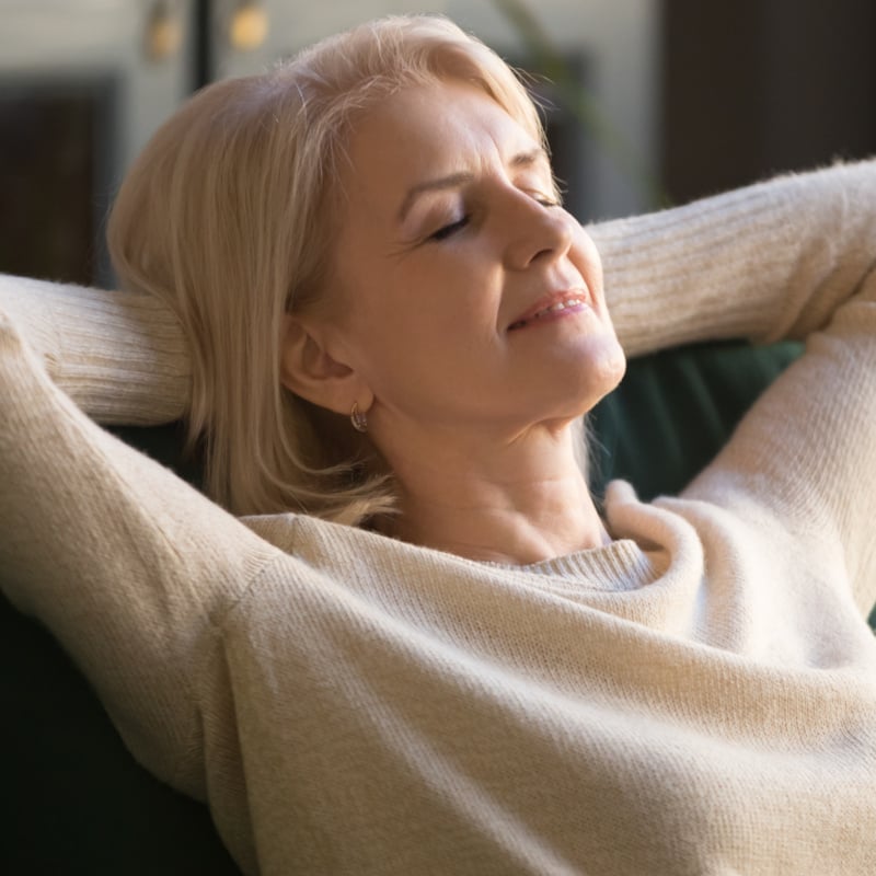 Calm happy old woman relaxing with eyes closed on couch