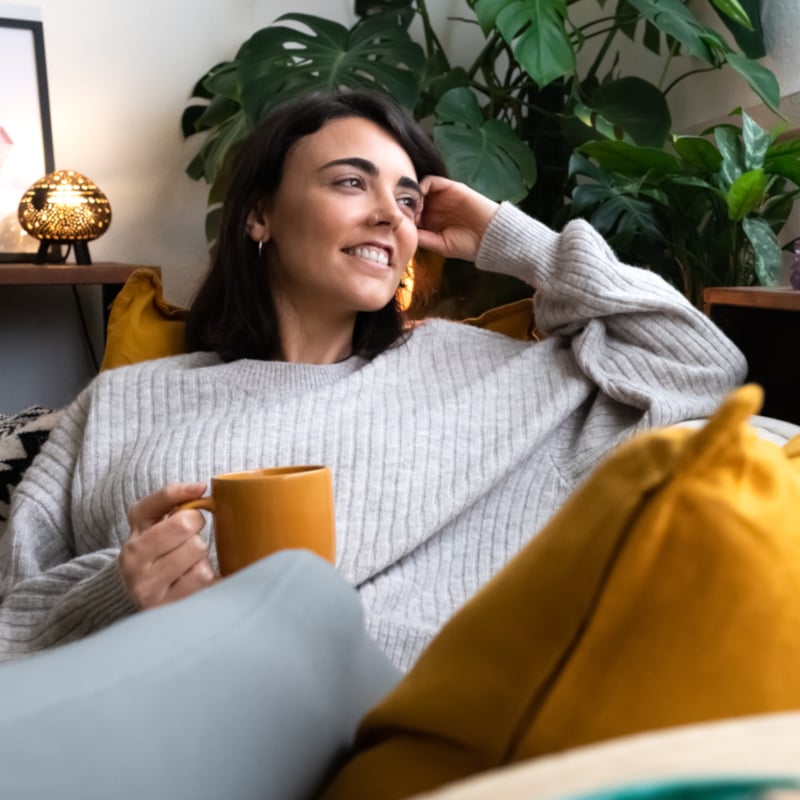 Happy young woman relaxing at home with tea looking out the window. Copy space.